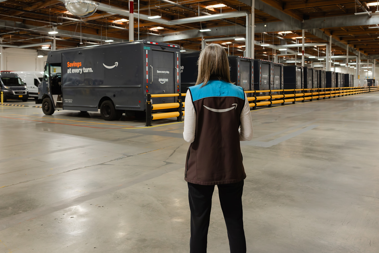 A Santosa Delivery team member standing before a line of delivery trucks in the warehouse.